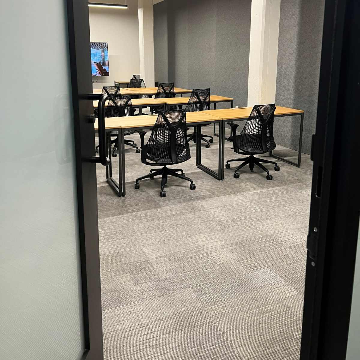 A modern conference room with several tables and black mesh chairs arranged neatly on a carpeted floor.