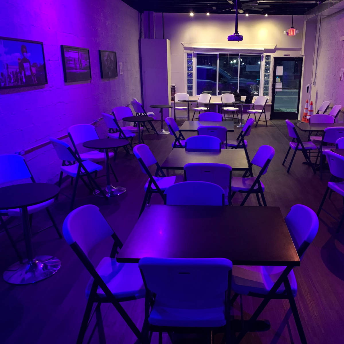 A dimly lit room with several folding tables and chairs arranged in rows, accompanied by framed photographs on the walls.