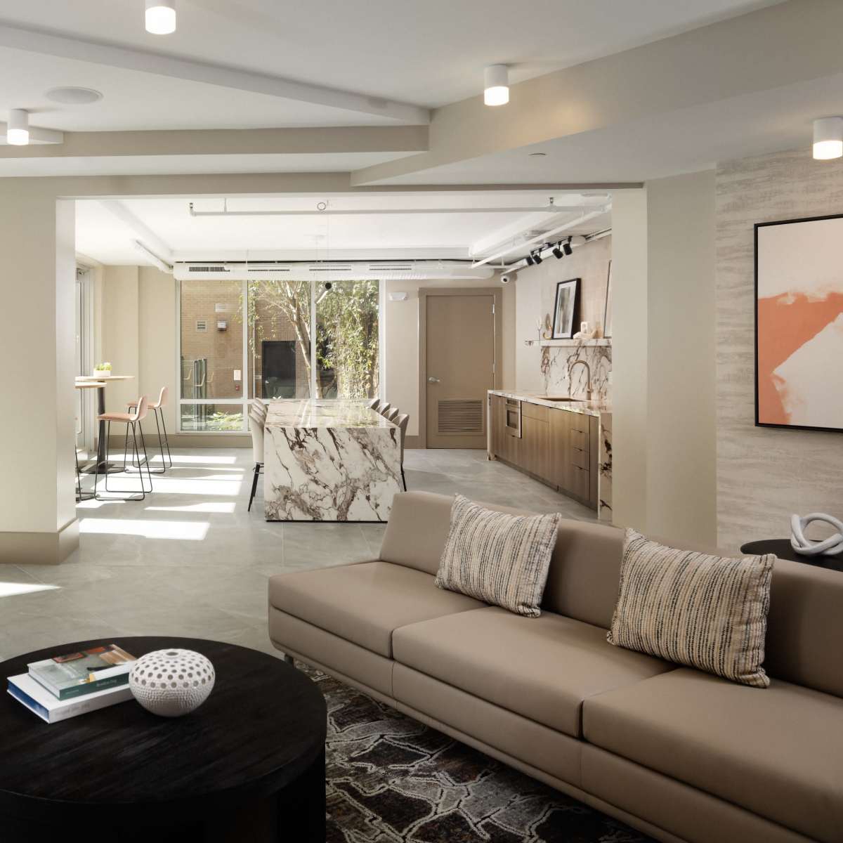 A modern, open-concept lounge area with a sectional sofa, a round coffee table, a dining space with chairs, and a kitchen in the background.