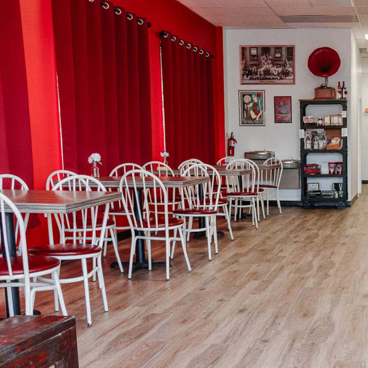 A café interior with red curtains, white tables and chairs, and a wooden counter along one side.