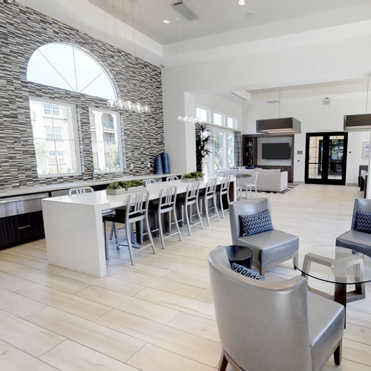 A modern communal space with a long dining table, several chairs, and large windows letting in natural light.