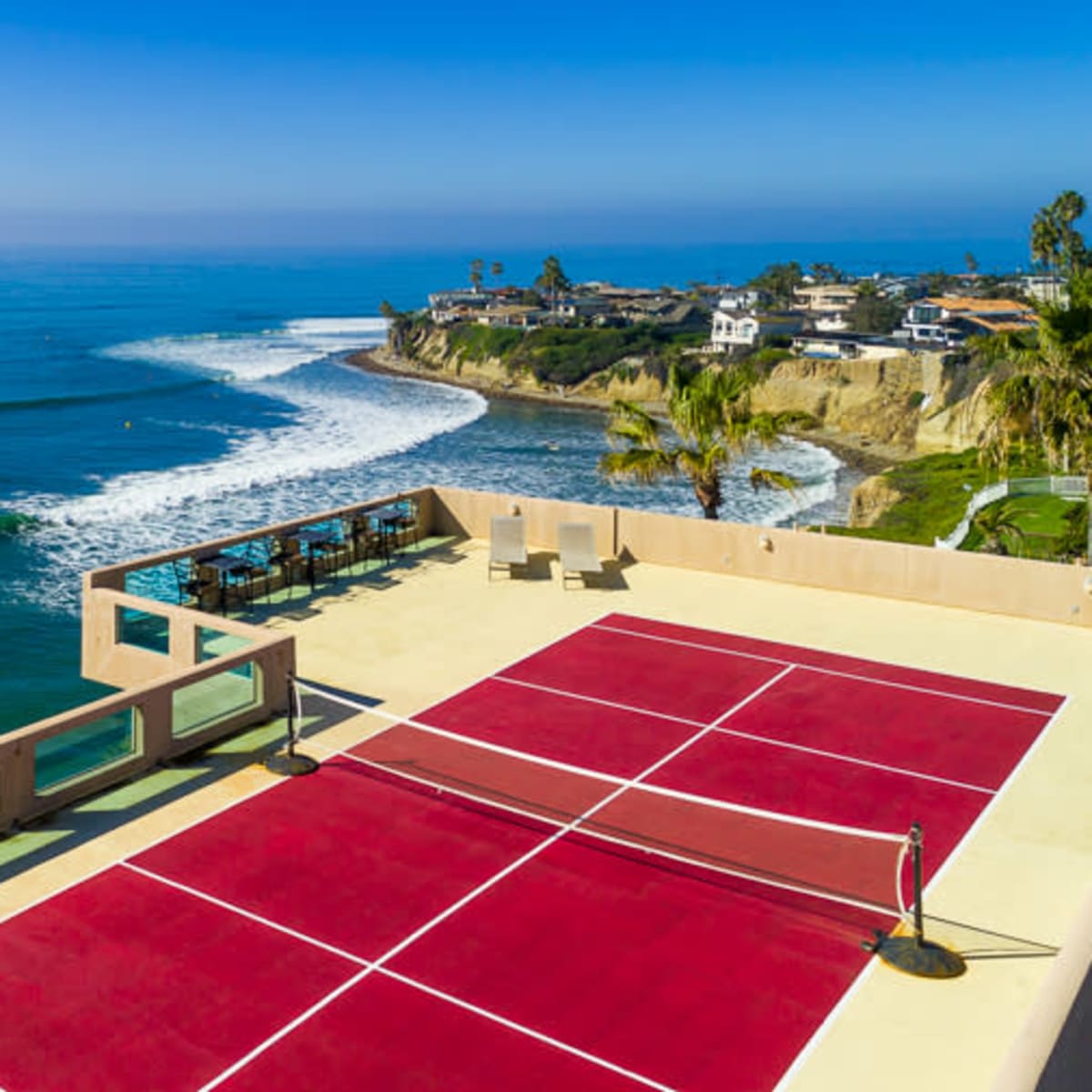 A seaside property with a red sports court overlooking a beach and ocean waves.