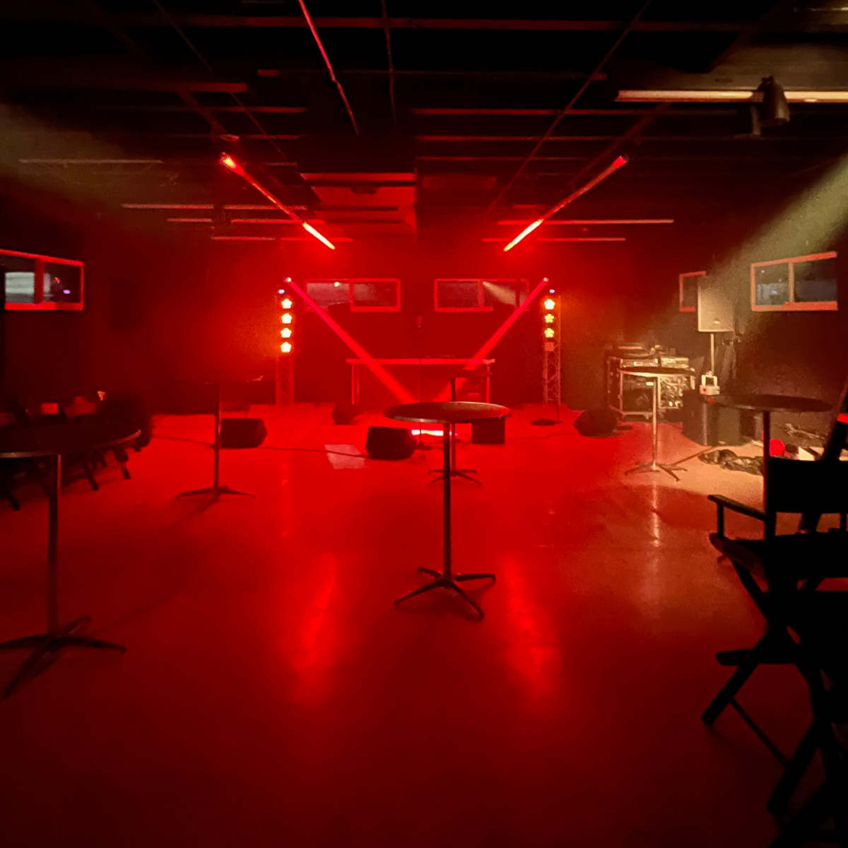 A dimly lit performance space featuring red stage lights, empty seating, and equipment positioned for a live event.
