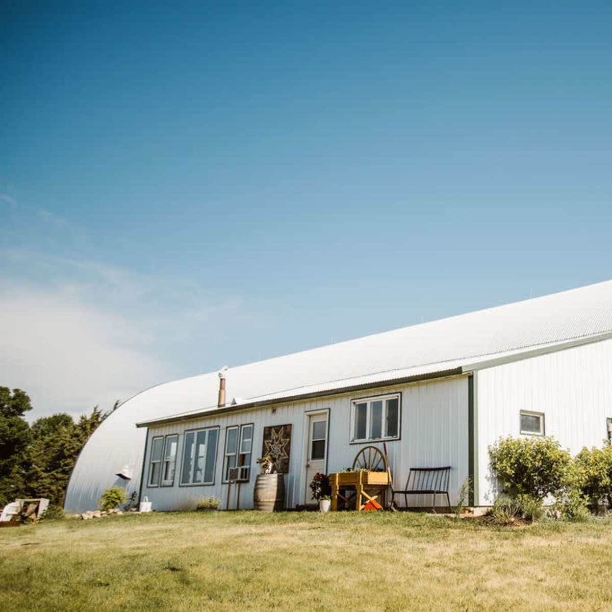 A large, white barn-style building with a curved roof set in a grassy landscape under a clear blue sky.