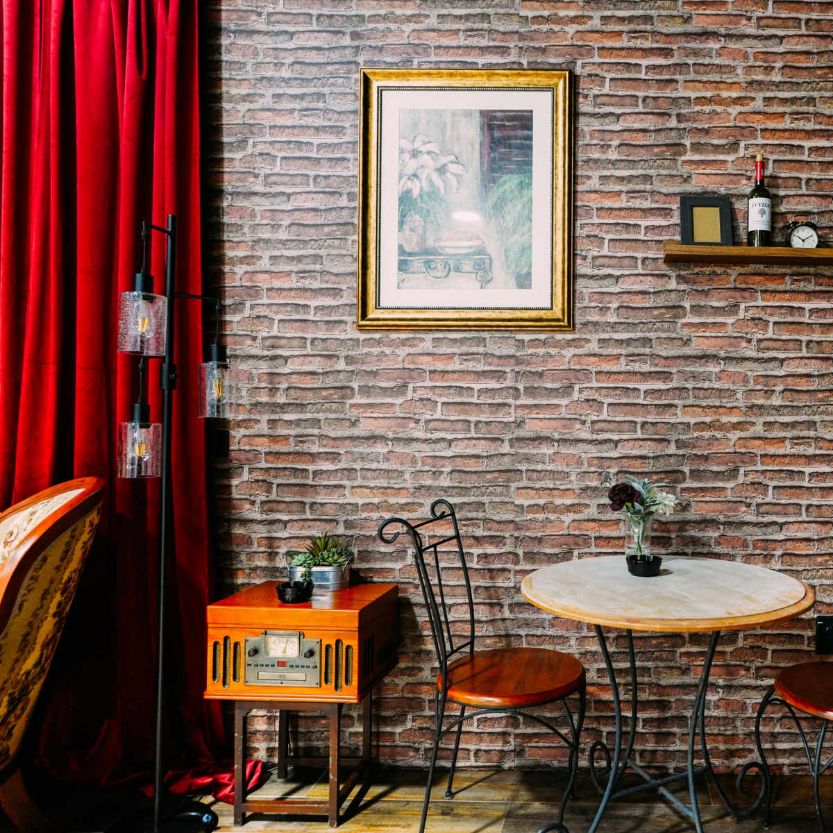 A bistro-style table with two chairs is arranged against a brick wall adorned with framed artwork and decorative items.