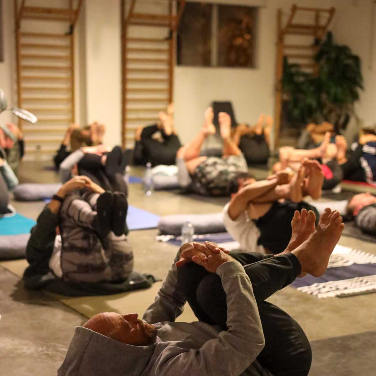 A group of people is practicing yoga in a studio, performing a pose while lying on mats.
