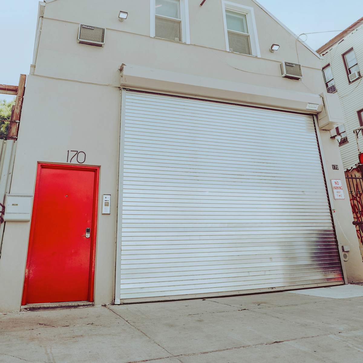 A building with a red door and a large silver roll-up garage door, set against a clear blue sky.