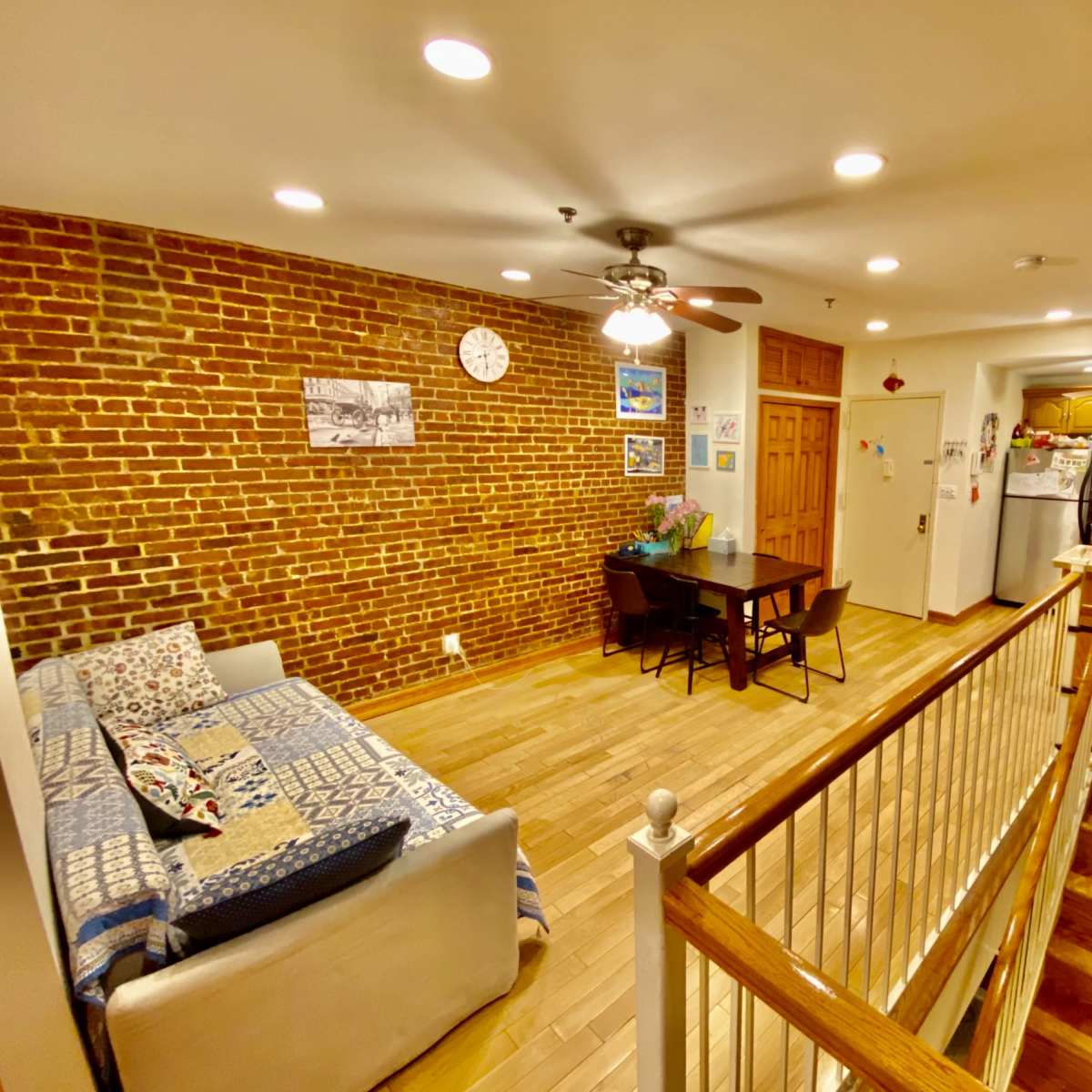 A spacious living area with exposed brick walls, a sofa, a dining table, and a kitchen visible in the background.