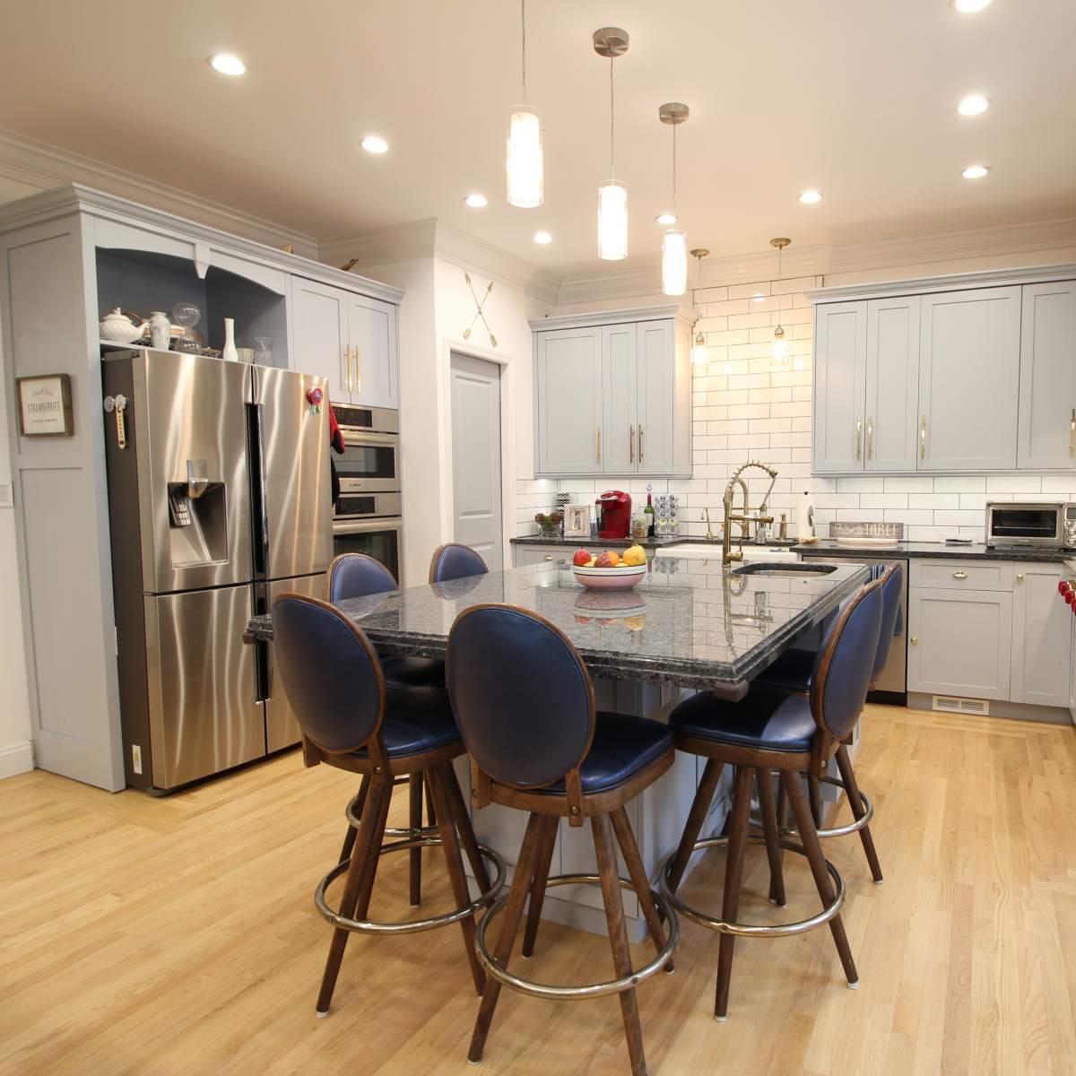 A modern kitchen with gray cabinetry, a large central island with bar stools, and stainless steel appliances.