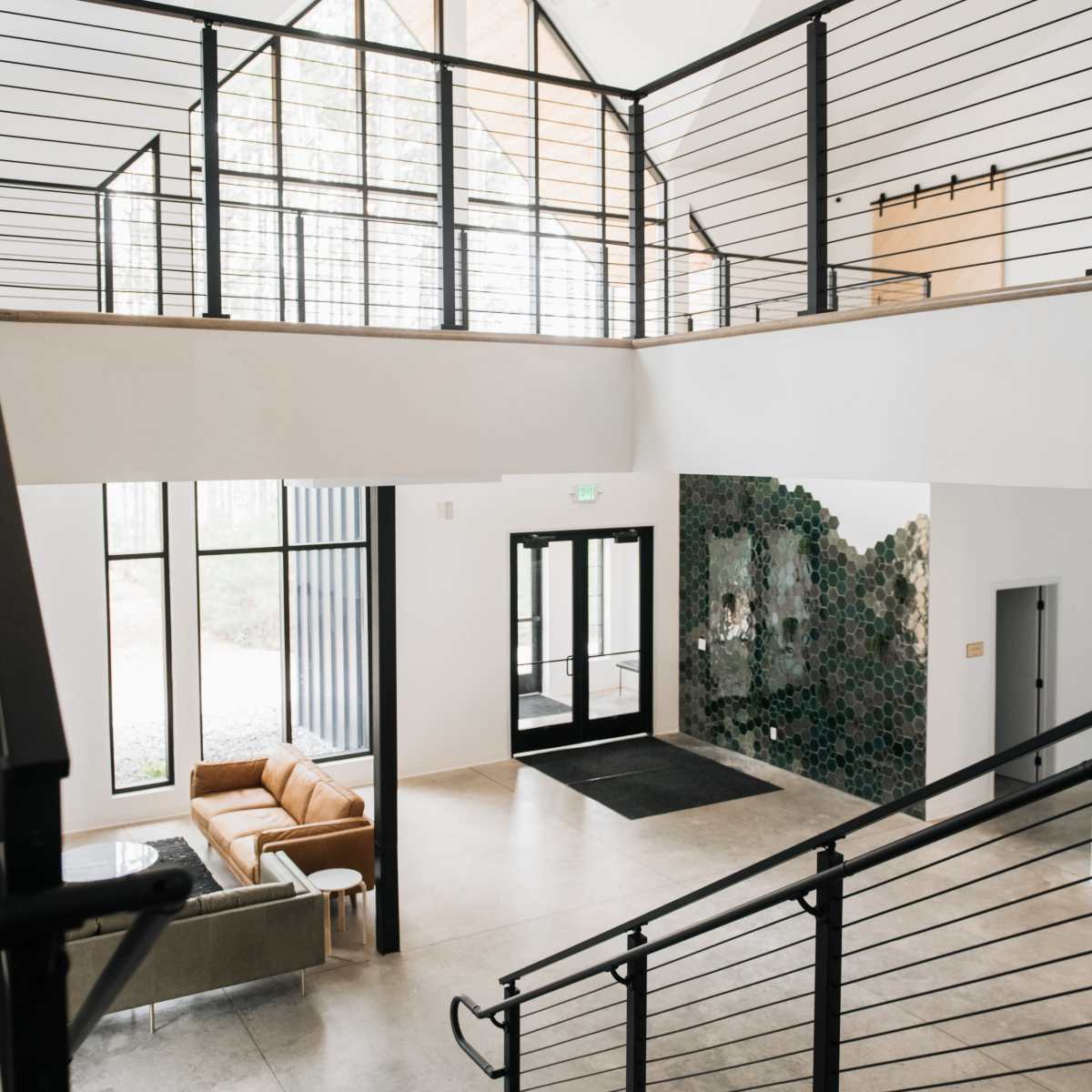 A modern entrance hall with a staircase, large windows, seating area, and decorative tile wall.