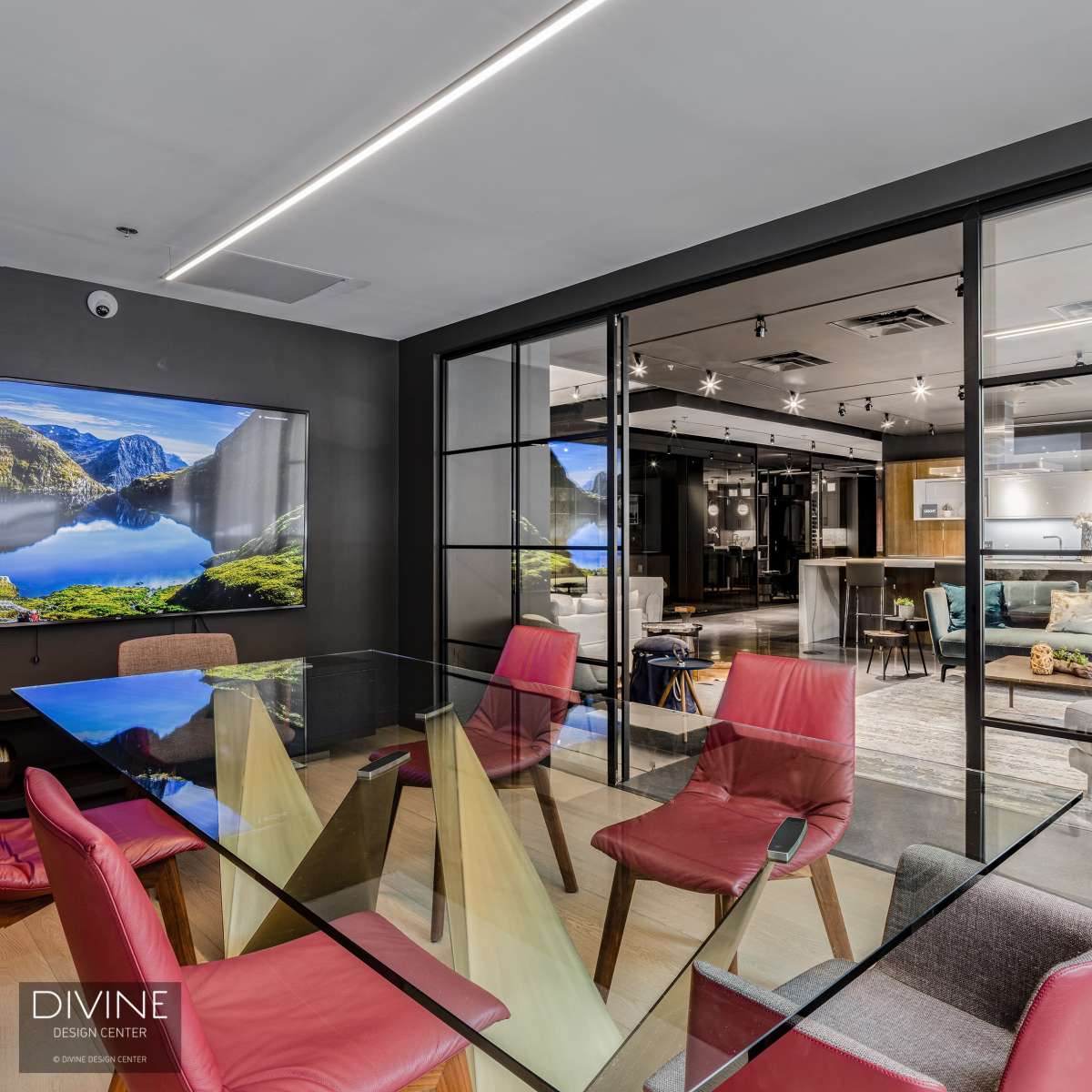 A modern meeting room features a glass table surrounded by colorful chairs, with a view of a contemporary open-plan living area in the background.