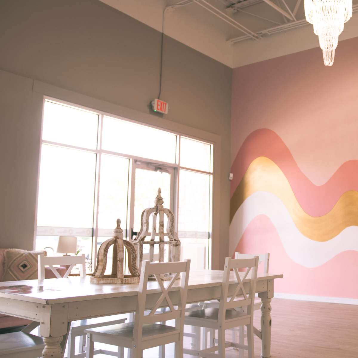 The scene features a spacious, well-lit room with a pink and gold wave-painted accent wall and a white dining table surrounded by chairs.