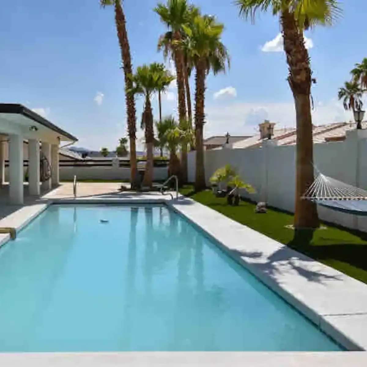 A swimming pool surrounded by palm trees and a white patio area.