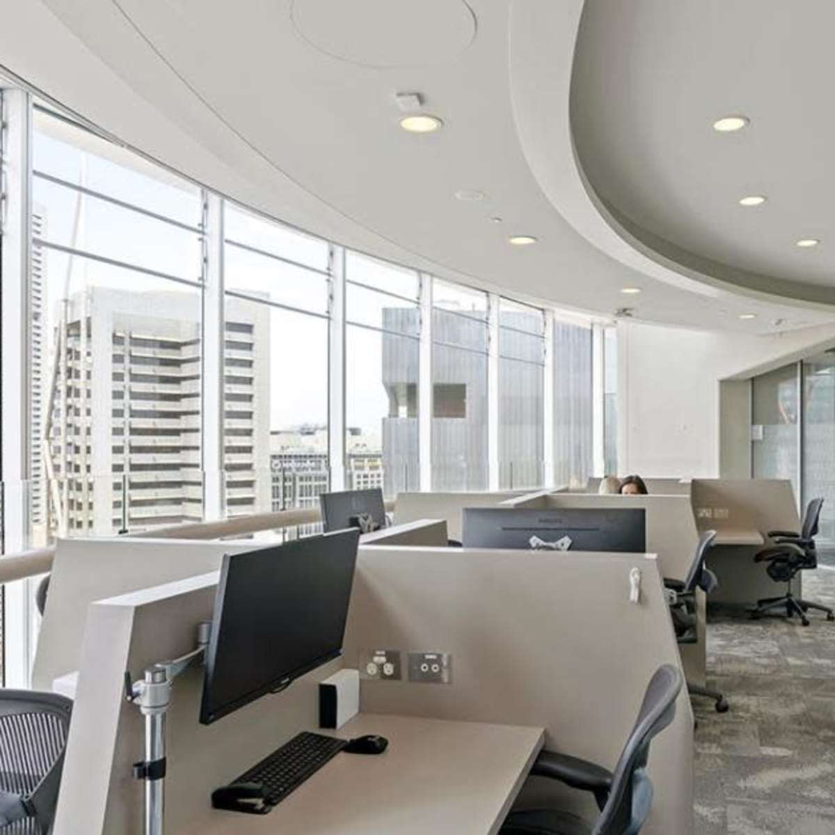 A modern office space with workstations, large windows, and a view of a skyline.