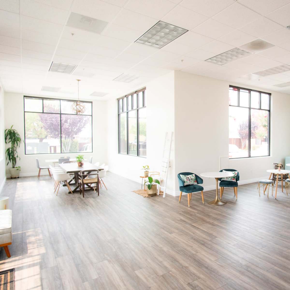 A spacious, well-lit office area with large windows, wooden flooring, and various seating arrangements.