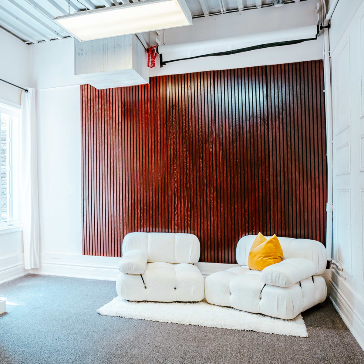 A bright room with a mirrored desk and a pair of white, textured lounge chairs against a wooden accent wall.