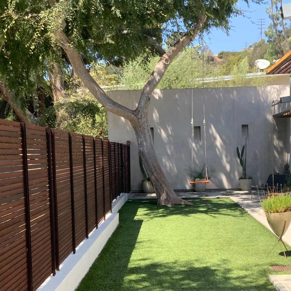 A landscaped area with artificial grass, a wooden fence, a tree, and a wall adorned with a hanging planter.