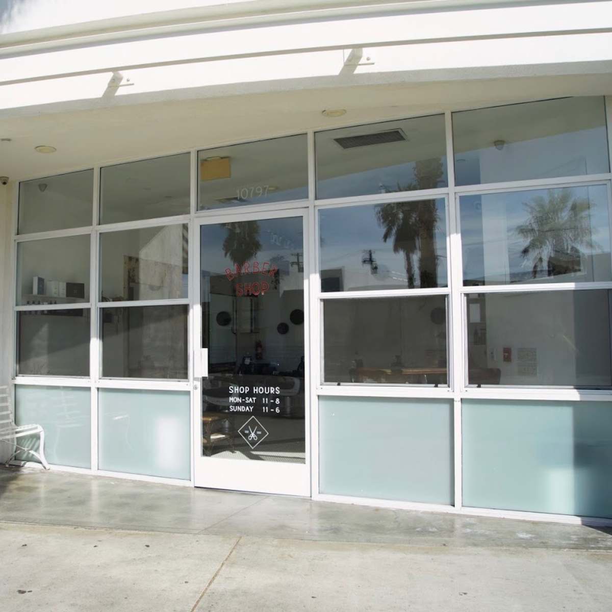 The storefront of a barbershop with large glass windows and a sign indicating shop hours.