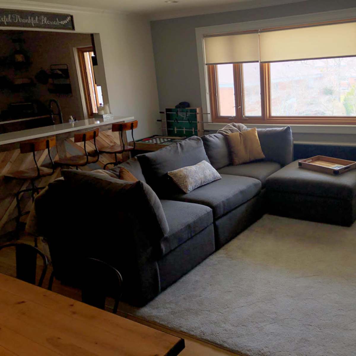 A modern living room with a large sectional sofa, a coffee table on a rug, and a window revealing an outdoor view.