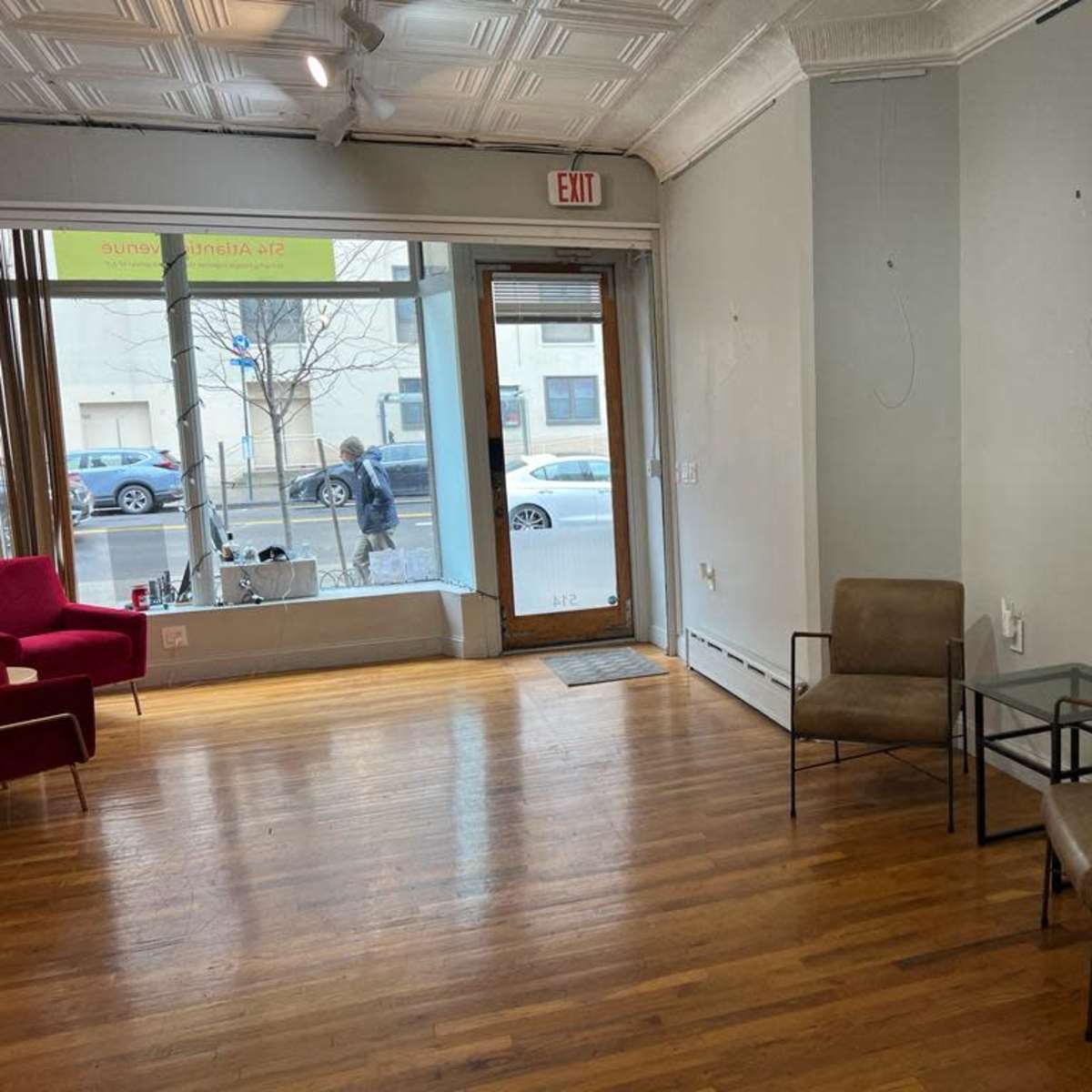 A brightly lit interior features two small chairs and a glass table, with a storefront window displaying a view of the street outside.