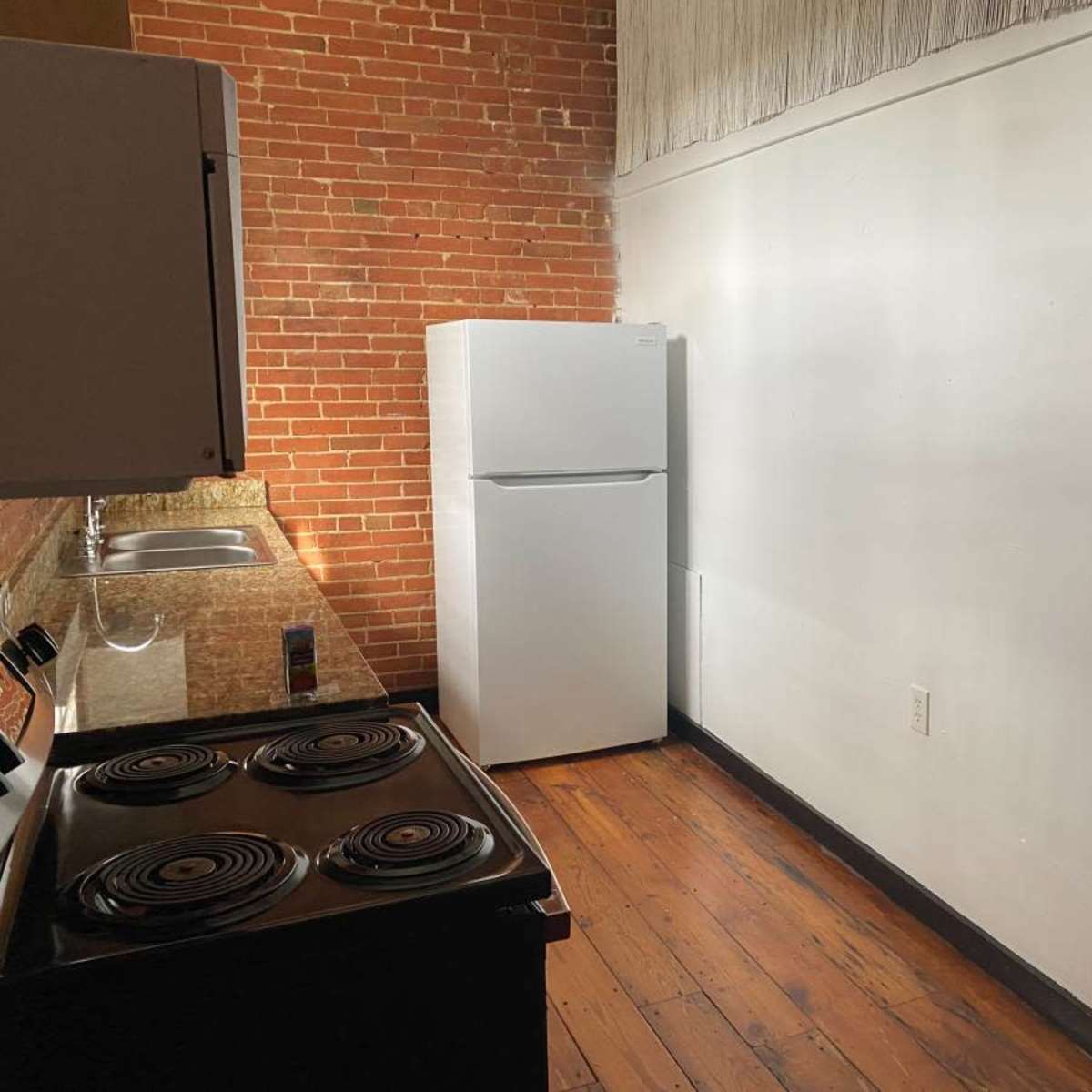 A kitchen with a white refrigerator, a stove, and exposed brick walls.