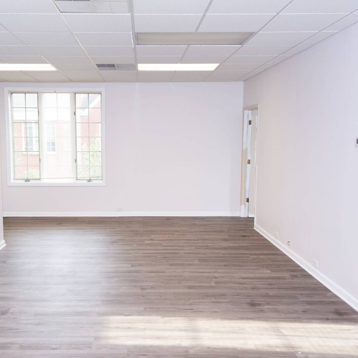 A vacant room with light-colored walls, a window, and hardwood flooring.