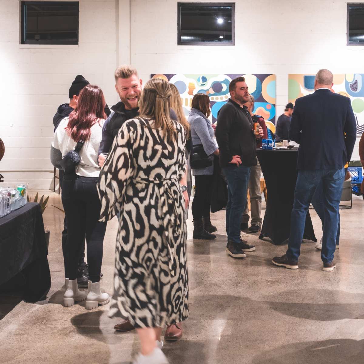 A group of people socialize at an indoor event in an art gallery with various artworks displayed on the walls.