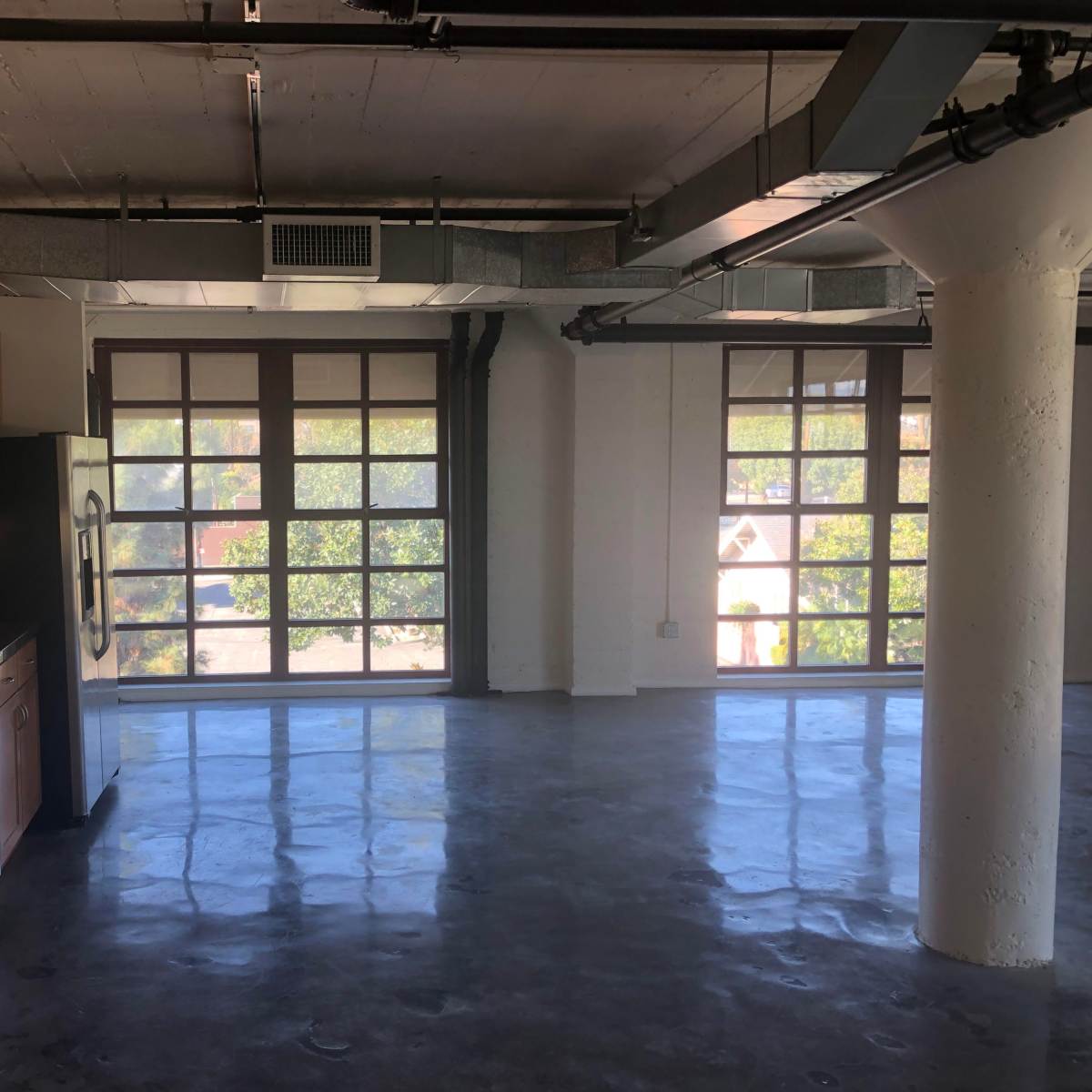 A spacious industrial kitchen area with wooden cabinets and a countertop, overlooking large windows in a modern apartment.