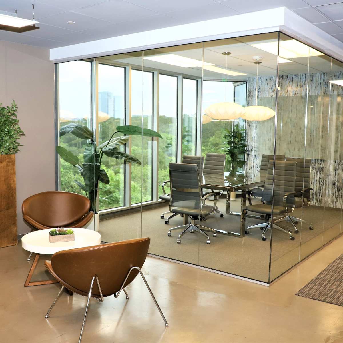 A modern office space features a glass-walled meeting room with a conference table and ergonomic chairs, surrounded by plants and soft lighting.