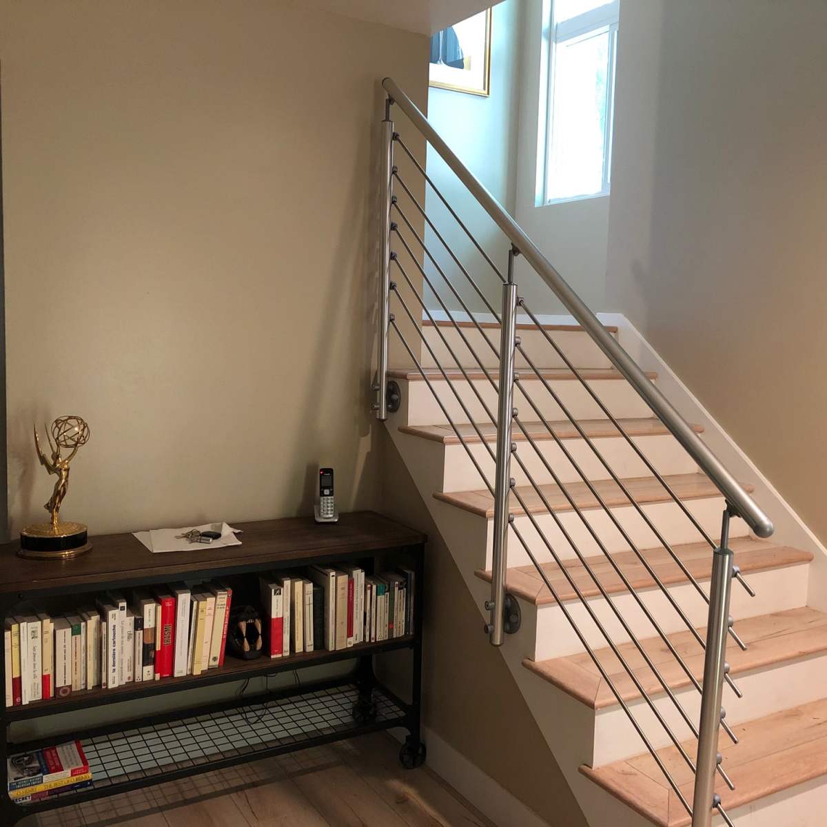 A staircase with a metal railing next to a wooden table holding books and a decorative item, against a wall painted in a light color.