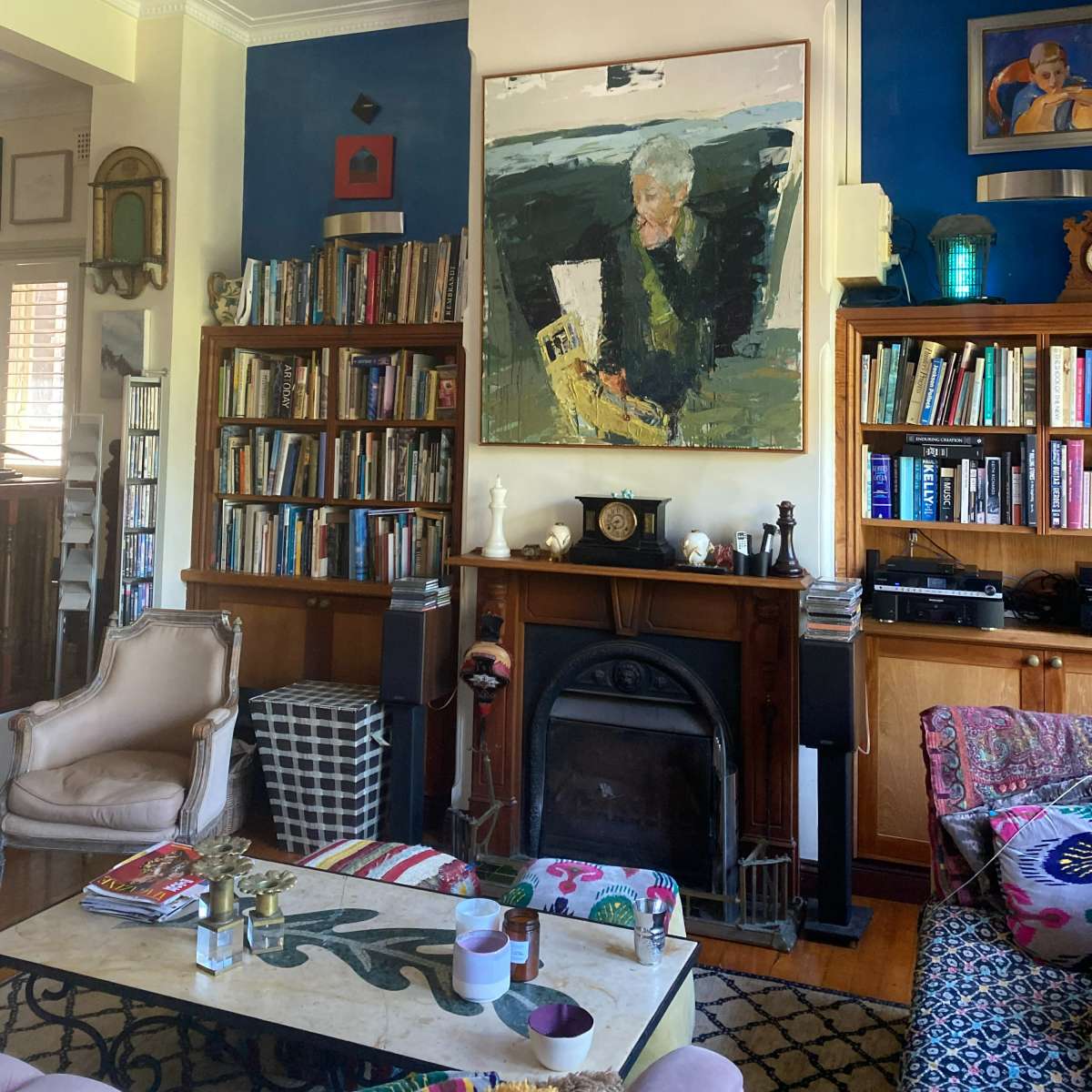 A living room with bookshelves, a fireplace, a large painting on the wall, and furniture arranged around a coffee table.