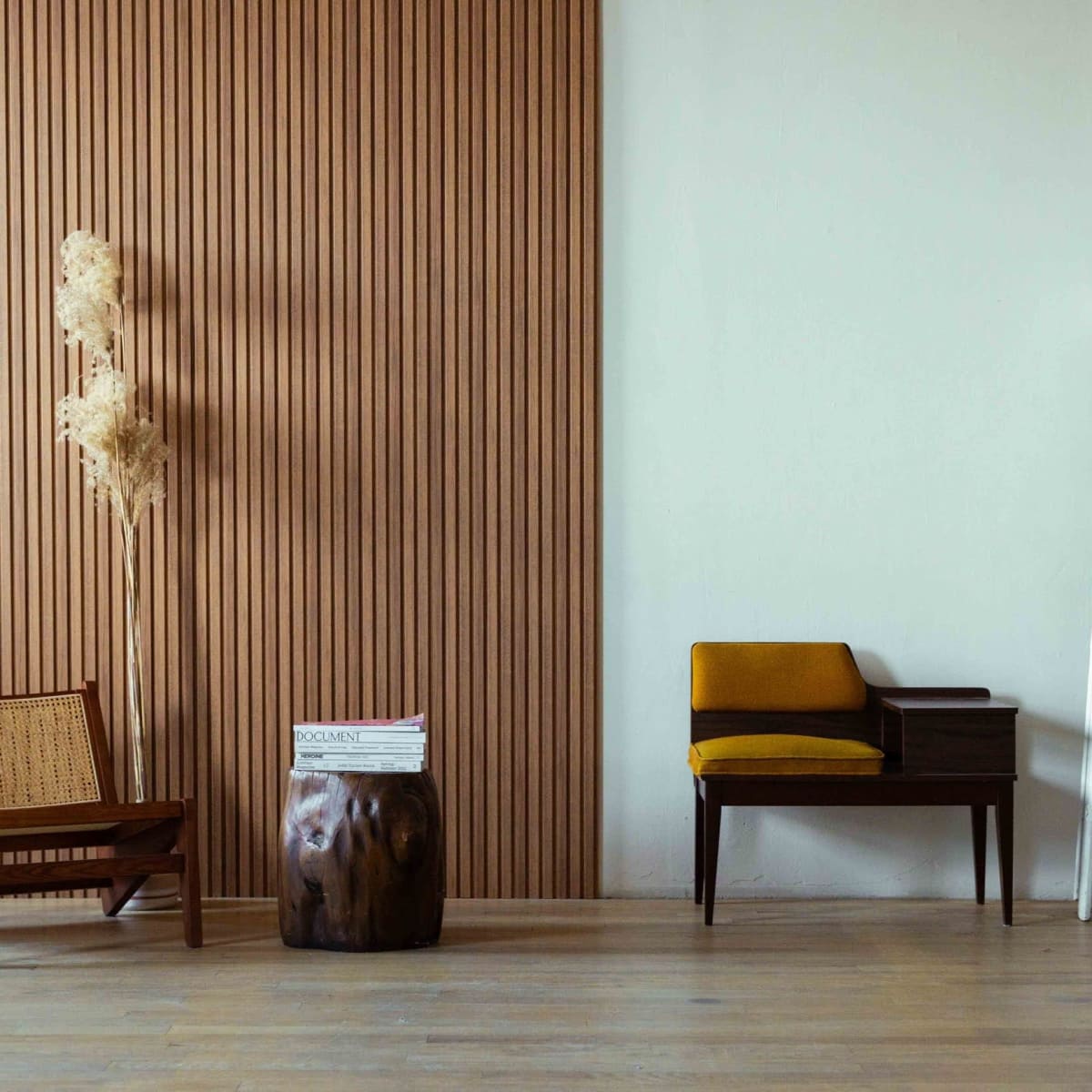 A minimalist interior featuring a wooden chair, a small table with a magazine, a potted plant, and a white ladder against a textured wall.