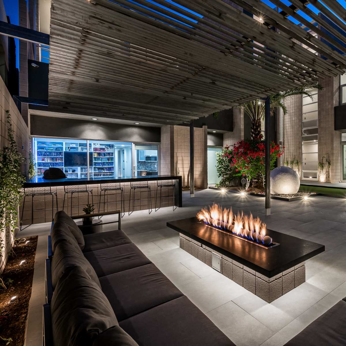 A modern outdoor living space featuring a fire pit with flames, surrounded by seating and illuminated by ambient lights in a sleek, contemporary design.