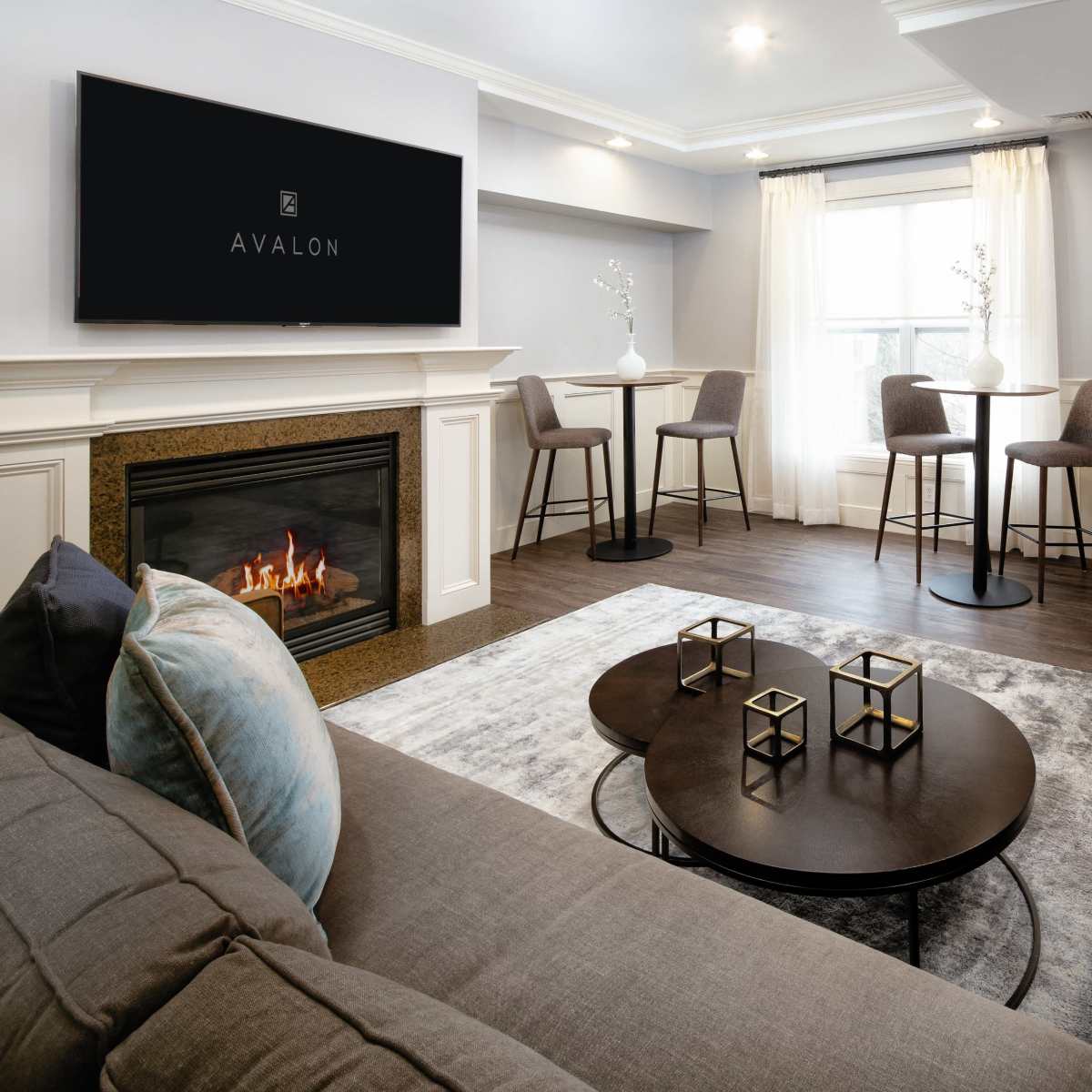 A modern living room with a fireplace, a cozy sofa, and a small dining area featuring high stools and a round table.