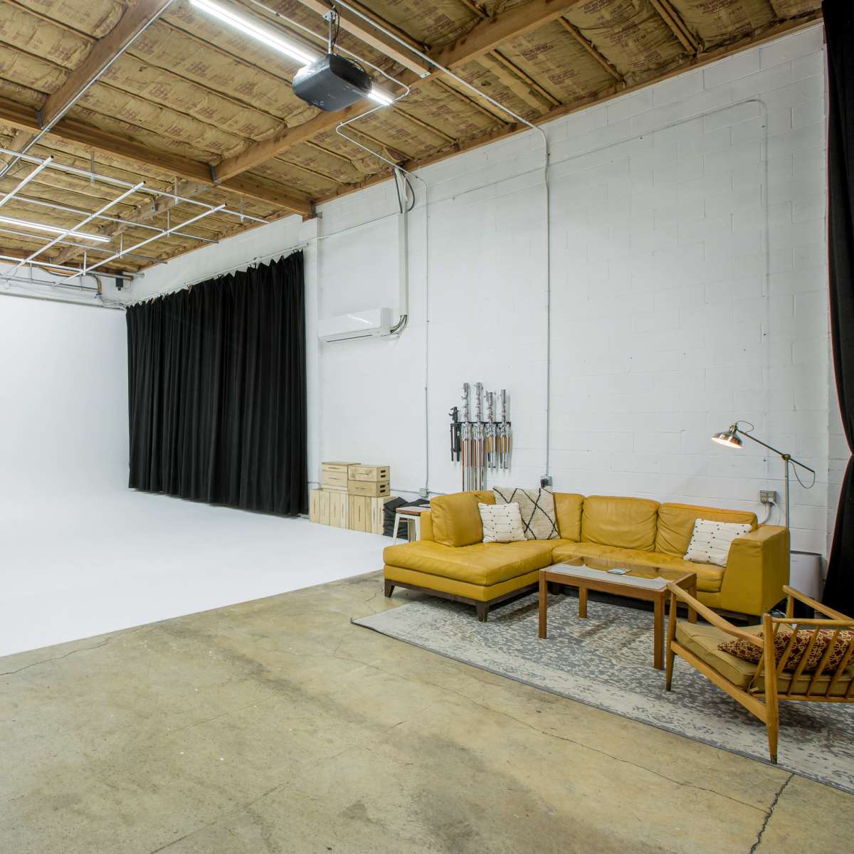 A spacious studio with a plain white backdrop, a dark curtain, a seating area with a sofa, and a small table.