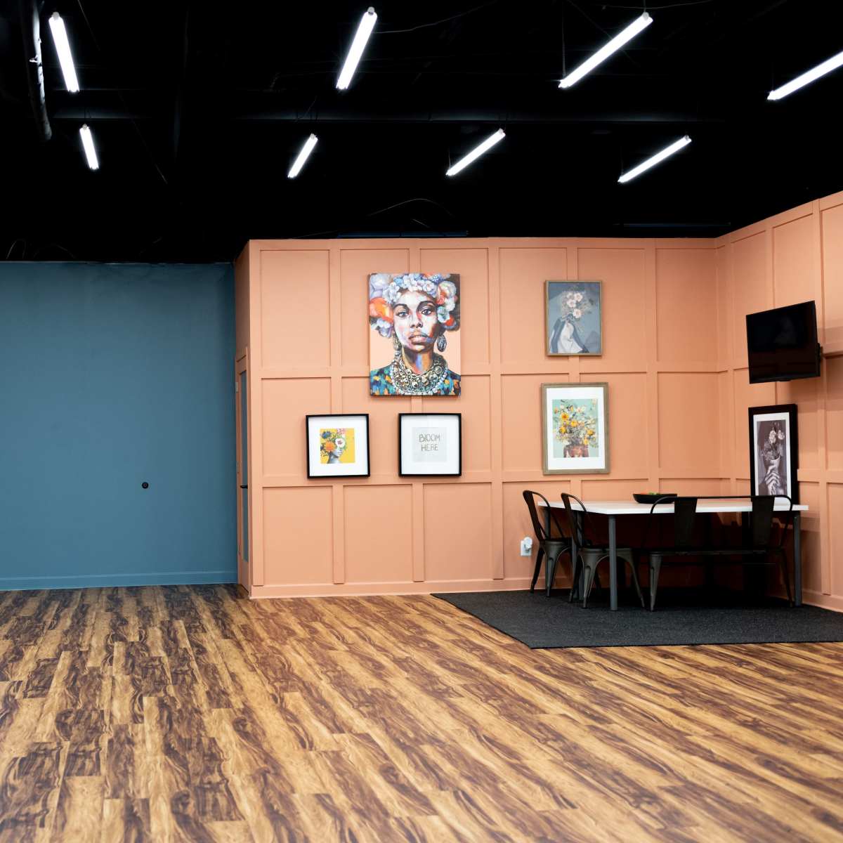 A spacious interior features a wooden floor, a blue wall with a doorway, and an orange-paneled wall displaying framed art.