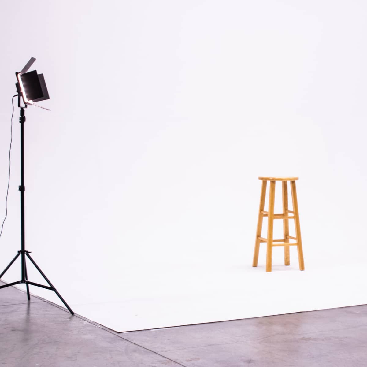 A wooden stool stands alone on a white backdrop in a studio setting.