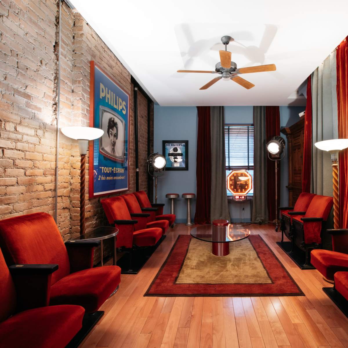 The room features vintage red velvet seating arranged along a wooden floor, with warm lighting and decorative curtains beside a framed advertisement on the wall.