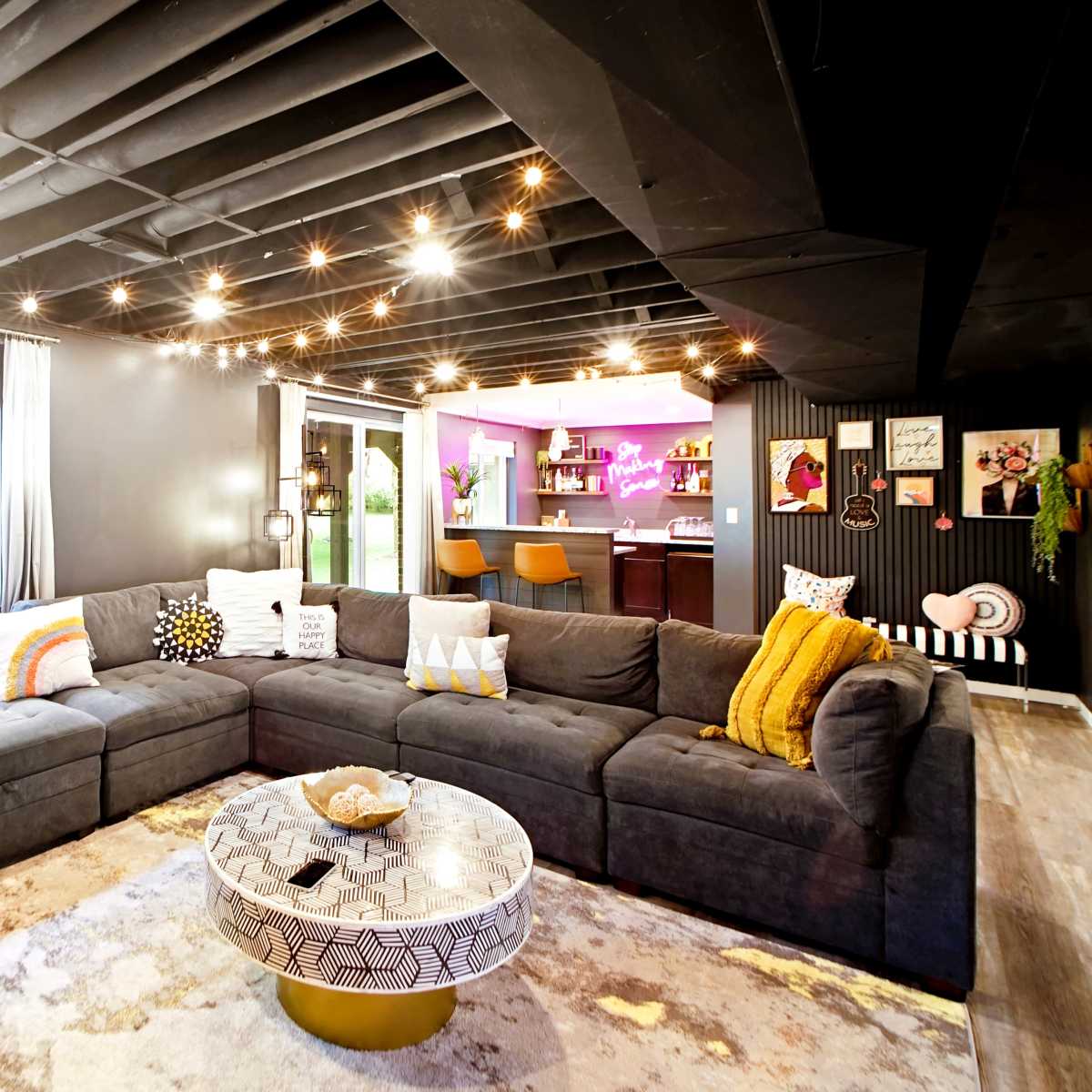 A modern living room with a large sectional sofa, a round coffee table, and a bar area illuminated by colorful lights.