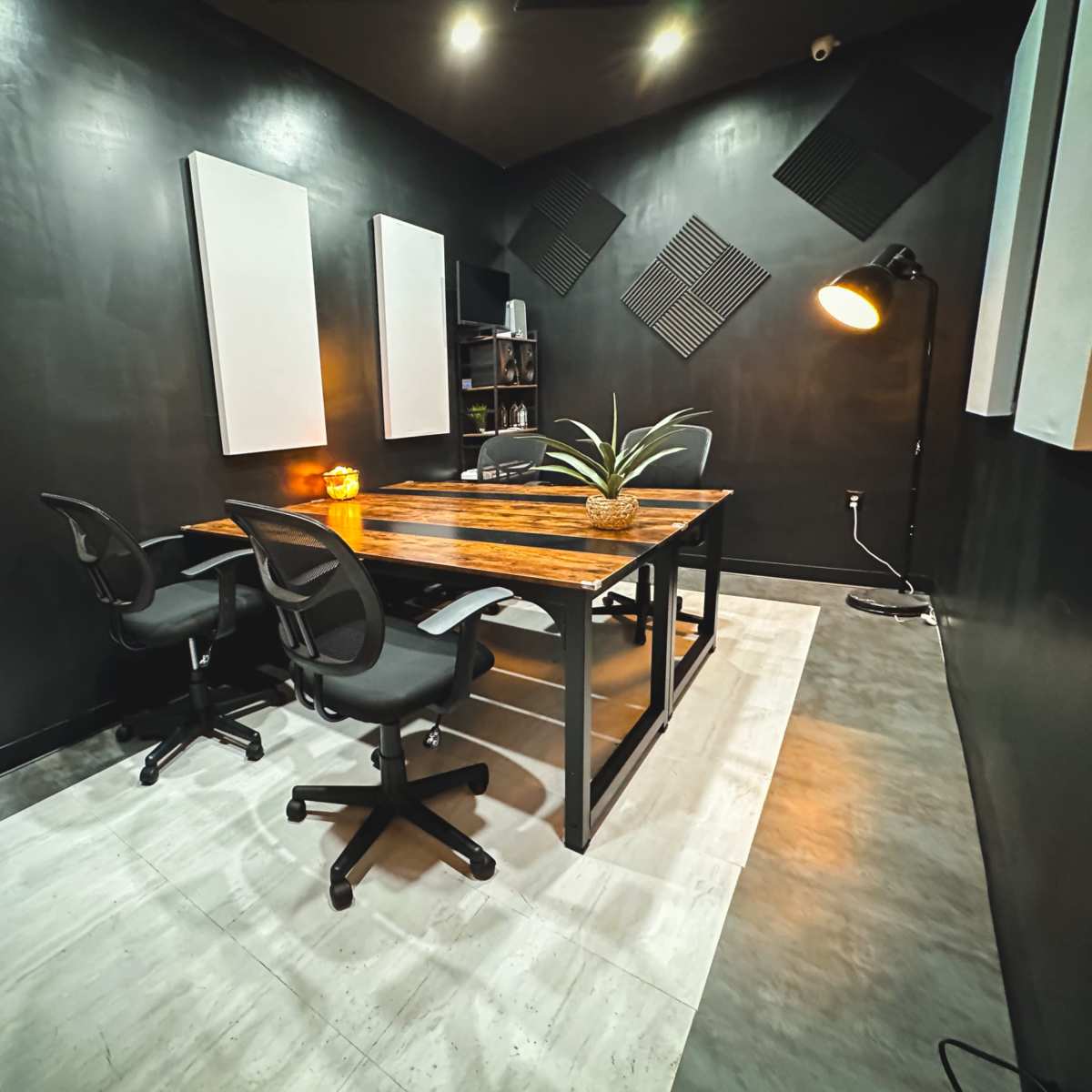 A small, modern meeting room features a wooden table with two chairs, soundproof panels on the walls, and a floor lamp in the corner.