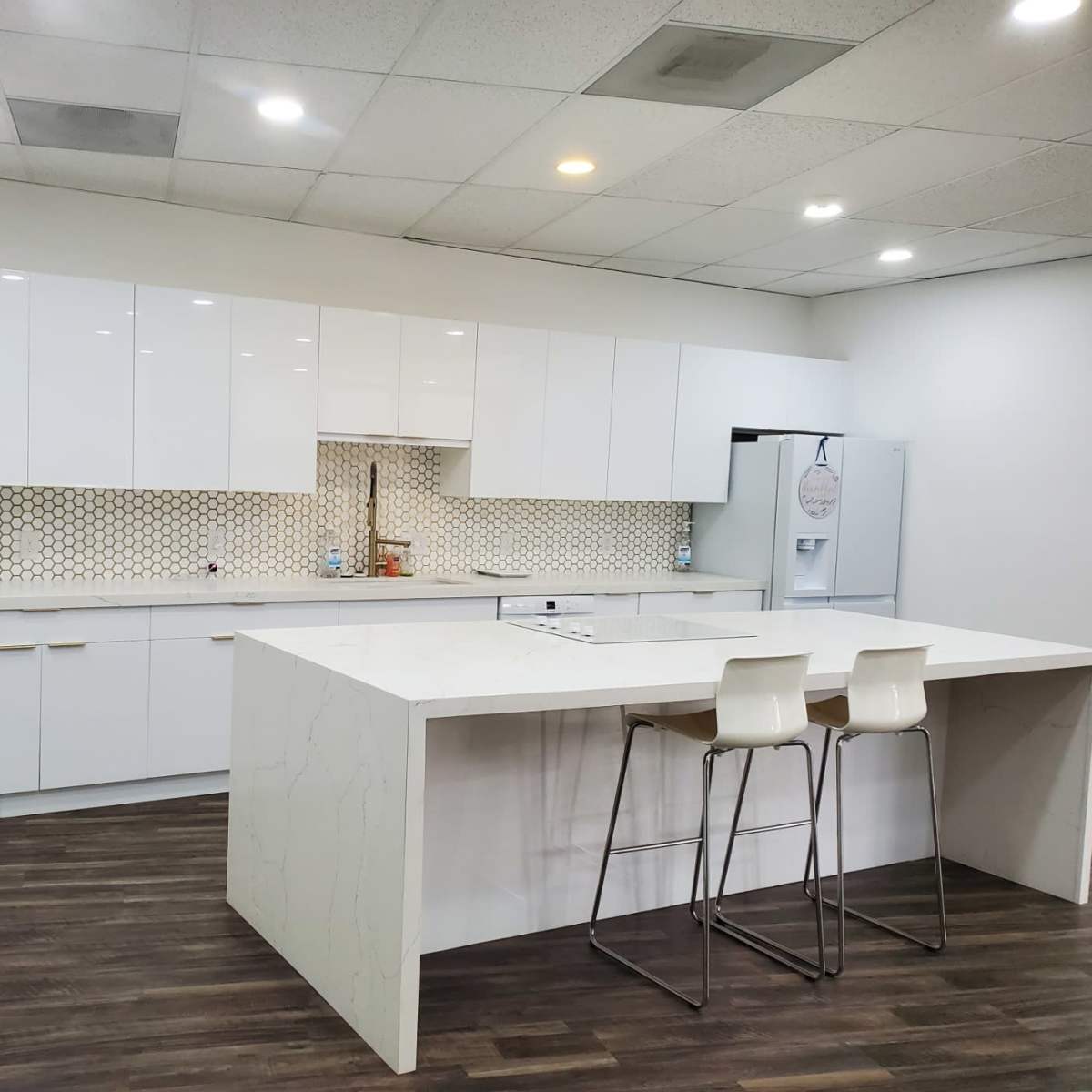 A modern kitchen with white cabinetry, a large island with seating, and a hexagonal tile backsplash.