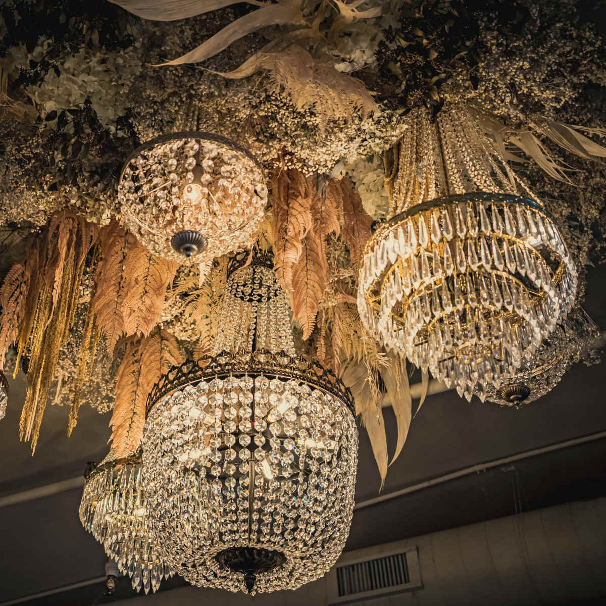 A collection of ornate chandeliers hanging from a ceiling adorned with dried floral arrangements.