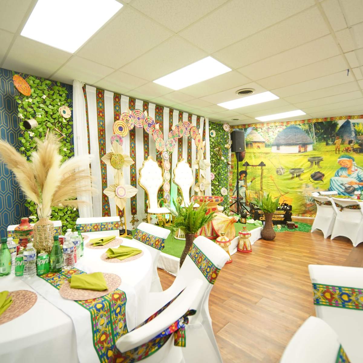 An elegantly decorated dining area with white tables, colorful table linens, and vibrant wall art featuring a pastoral scene.