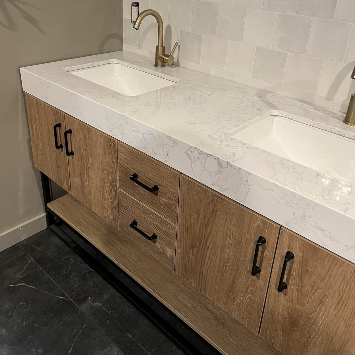 A modern bathroom vanity with a marble countertop, two sinks, and wooden cabinetry below.