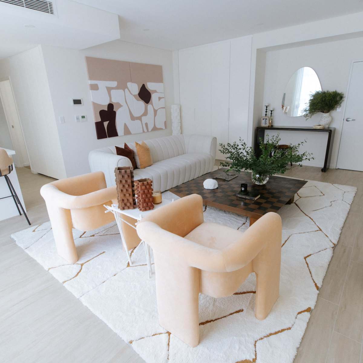 A modern living room with a white sofa, two accent chairs, a coffee table, and a decorative rug, all arranged around a plant centerpiece.