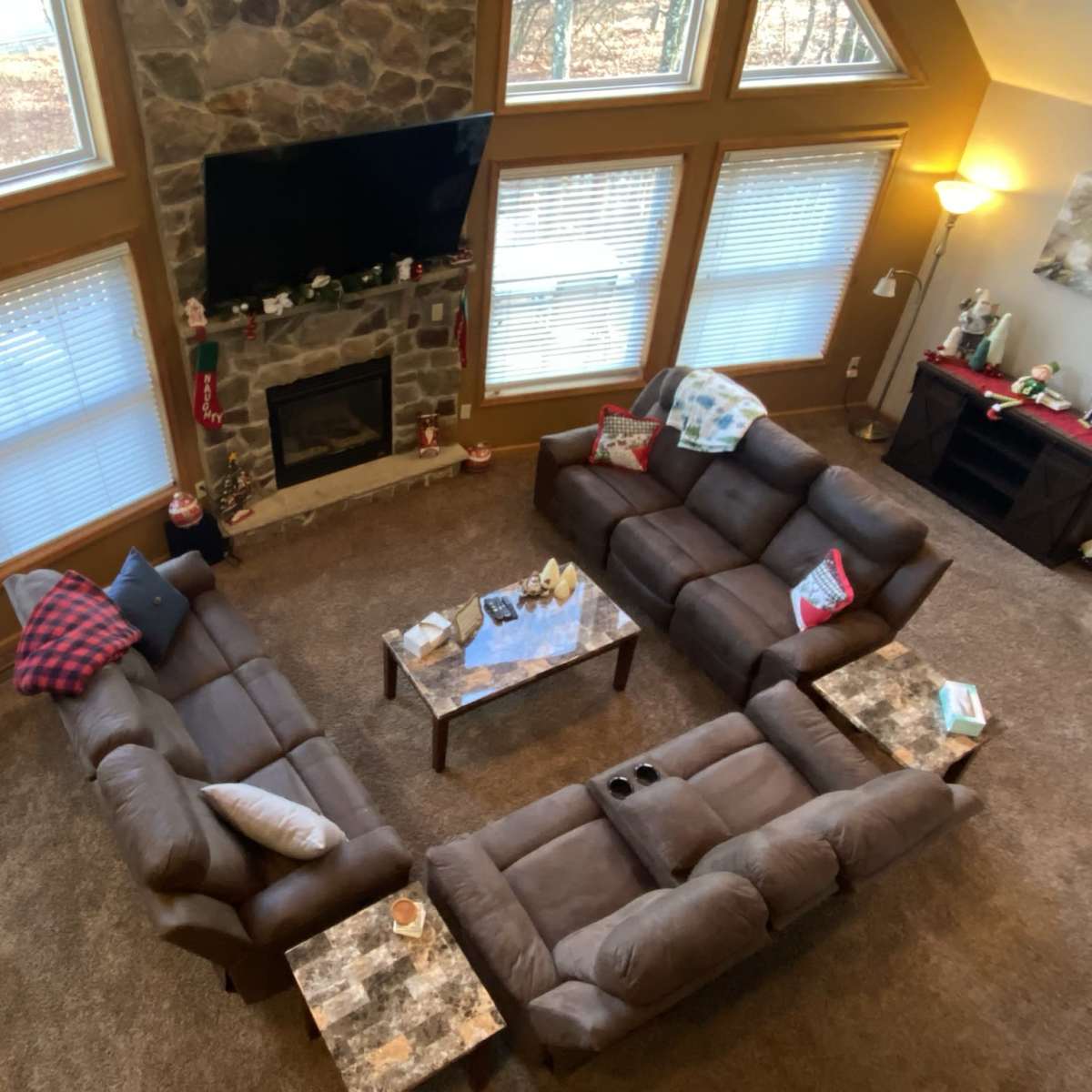 A living room with two sectional sofas arranged in a U-shape around a coffee table, a stone fireplace, and a Christmas tree in the corner.