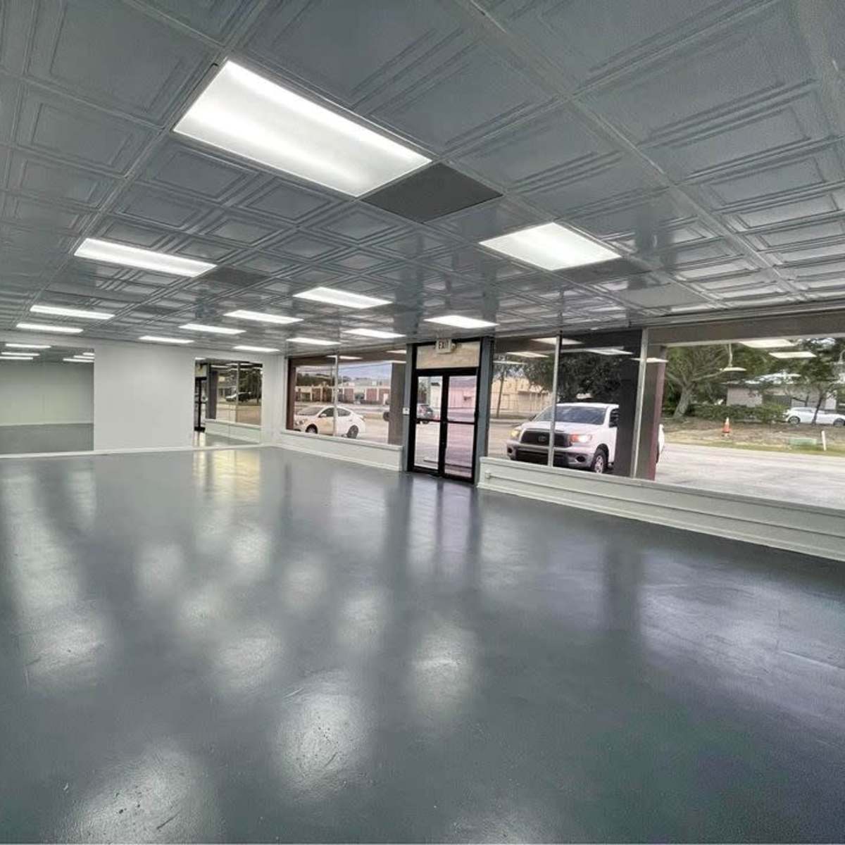 An empty commercial space with a gray floor, white walls, and large front windows.