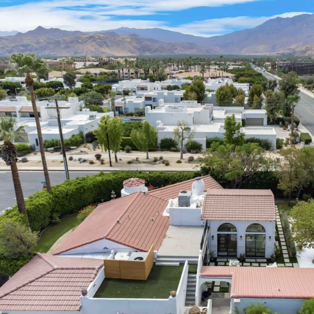 An aerial view of a residential area featuring houses, palm trees, and a swimming pool surrounded by mountains.