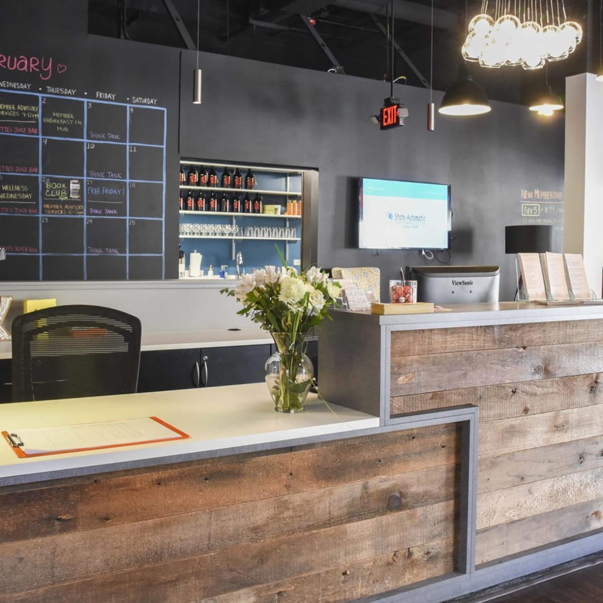 A modern reception area with a wooden front desk, a calendar on the wall, and a floral arrangement on the counter.