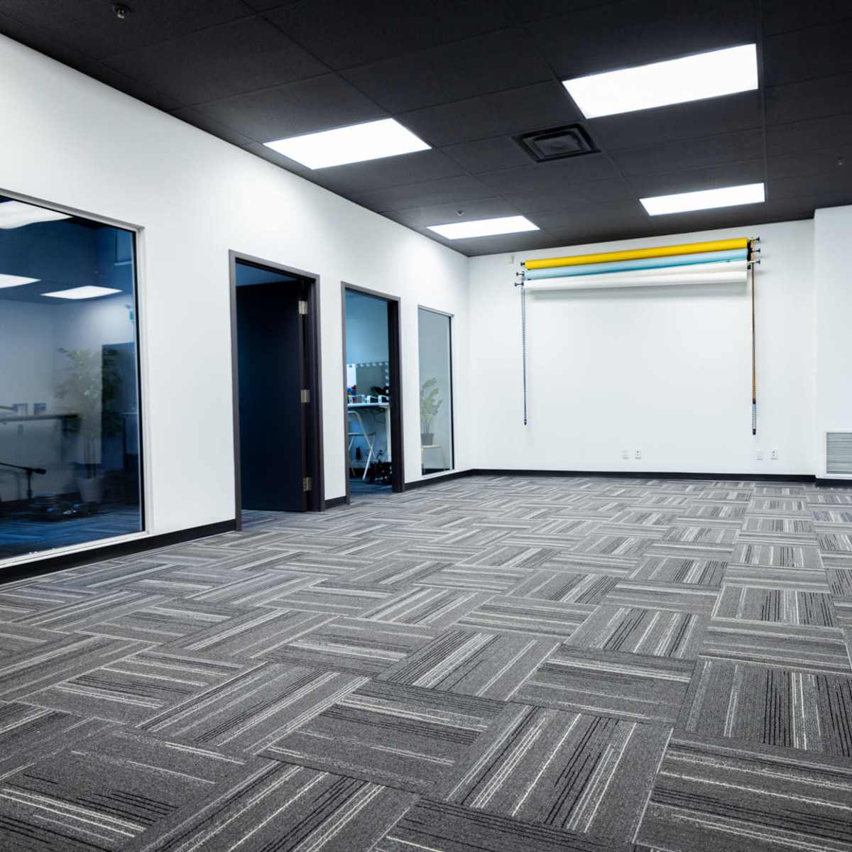 A spacious empty office room with patterned carpet, white walls, and three doorways leading to adjacent rooms.